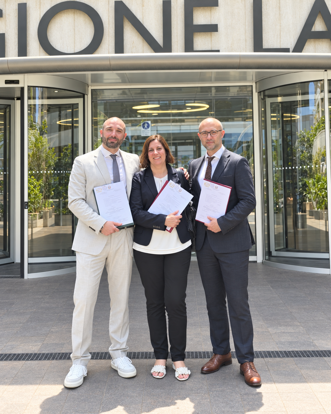 Tre persone con documenti in mano davanti a un ingresso a vetri.
